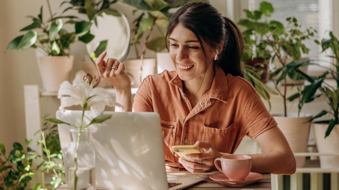 Woman working on a laptop at a desk surrounded by green plants