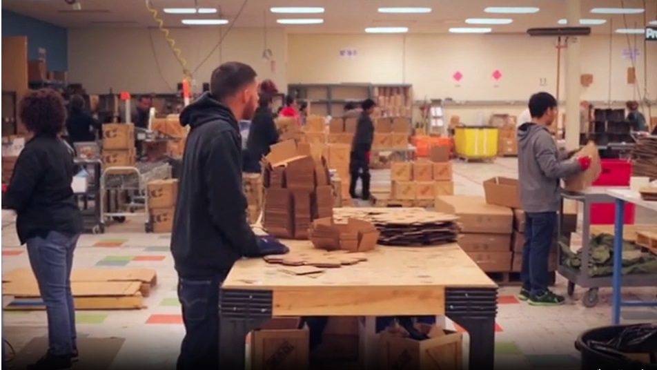 video still of workers in a warehouse moving cardboard boxes