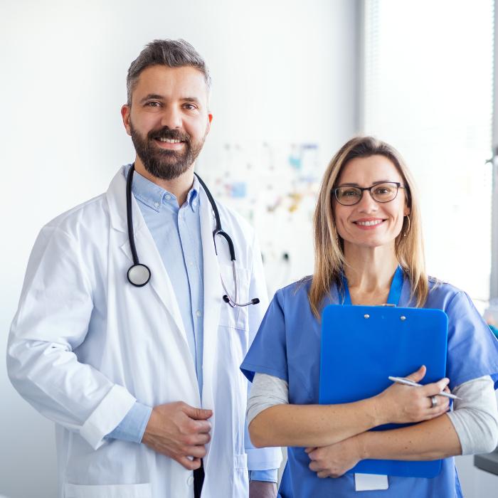 man in a doctor coat and woman in blue scrub top smiling 