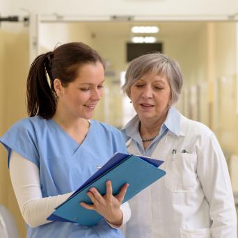 woman in a blue scrub top looking at a clipboard with an elderly woman 