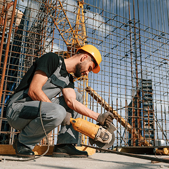 construction worker in a yellow hard hat cutting materials with a saw machine