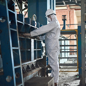 worker in a full white body suite and white hard hat looking into blue metal shelves