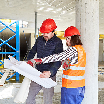 two construction workers in red hard hats looking at construction plans