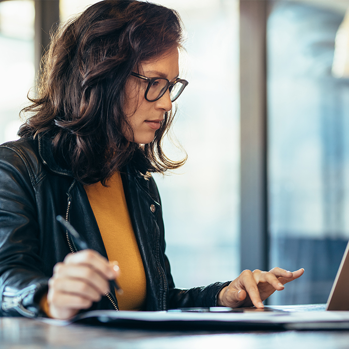 woman working at a laptop while writing on a notepad