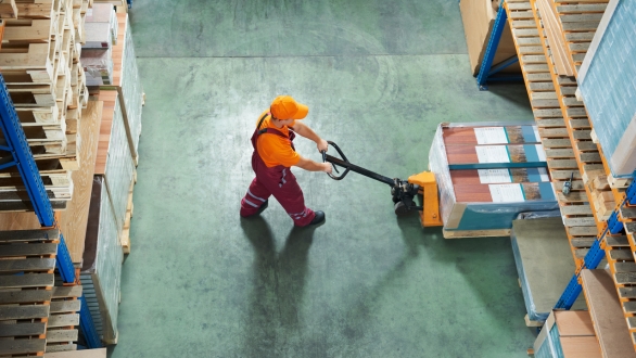 Warehouse working using a power jack to move a box through the warehouse.