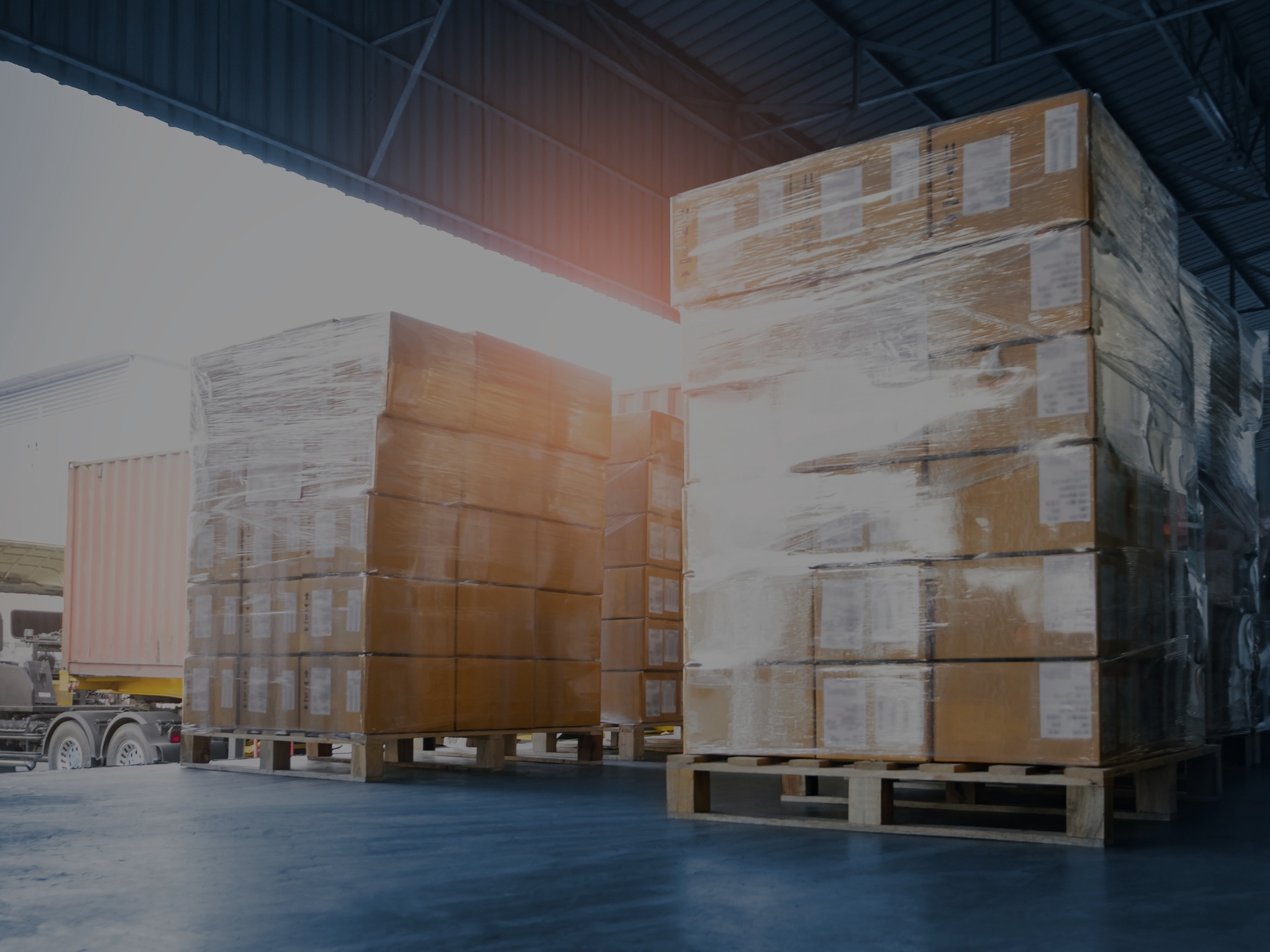 Sunlight shining through pallets of wrapped boxes on a loading dock. 