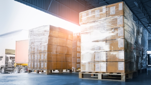 Sunlight shining through pallets of wrapped boxes on a loading dock. 